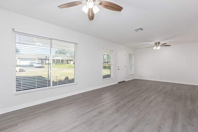 unfurnished room with ceiling fan, wood finished floors, visible vents, and baseboards