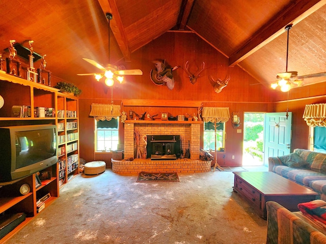 carpeted living room with wood walls, ceiling fan, beam ceiling, and a fireplace