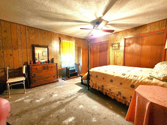 carpeted bedroom featuring ceiling fan, a textured ceiling, wooden walls, and two closets