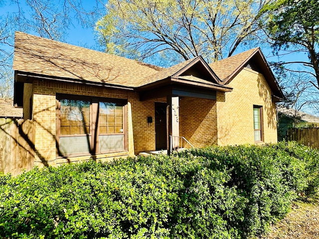 ranch-style house with a shingled roof, fence, and brick siding