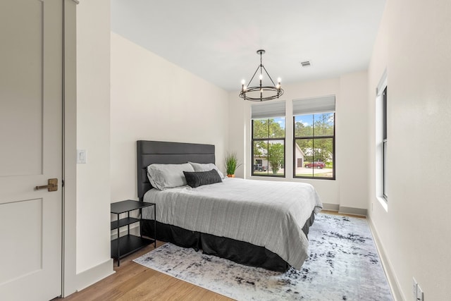 bedroom with baseboards, light wood-style flooring, a chandelier, and visible vents