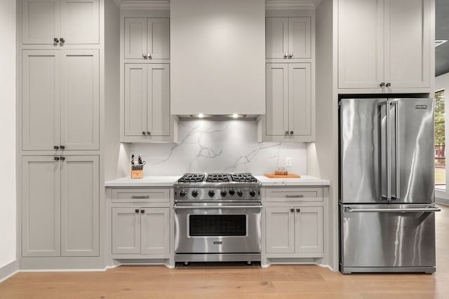 kitchen with light countertops, light wood-style flooring, high end appliances, and decorative backsplash