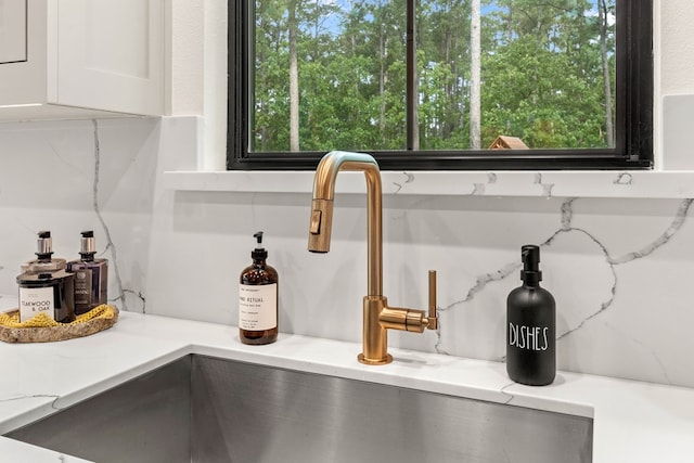 room details with white cabinets, light stone countertops, a sink, and tasteful backsplash