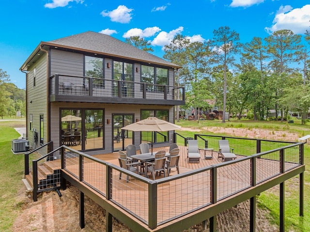 rear view of house with outdoor dining space, a shingled roof, central AC unit, a balcony, and a lawn