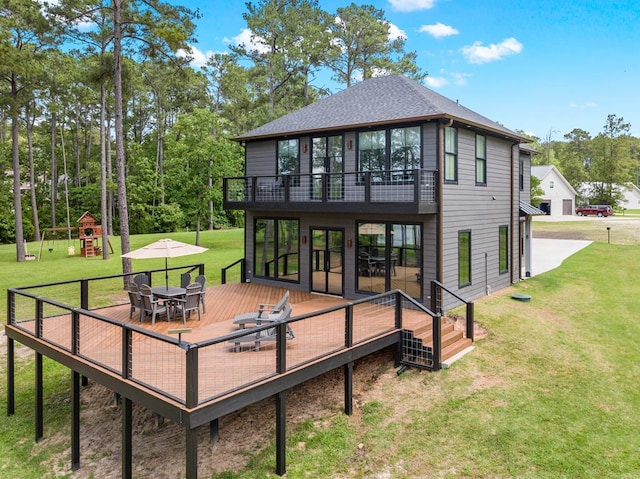 rear view of property featuring a deck, roof with shingles, a playground, a lawn, and outdoor dining space