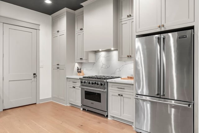 kitchen with decorative backsplash, high end appliances, light wood-type flooring, light countertops, and recessed lighting