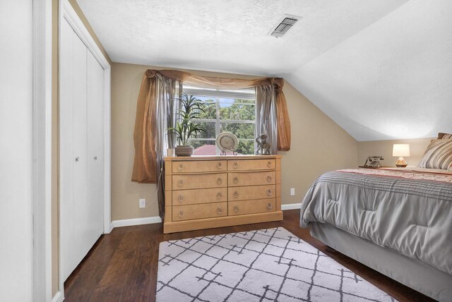 bedroom featuring a textured ceiling, vaulted ceiling, a closet, and dark wood-type flooring