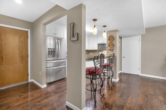 kitchen featuring appliances with stainless steel finishes, a textured ceiling, pendant lighting, dark hardwood / wood-style floors, and white cabinetry