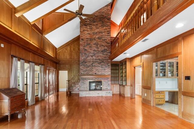 unfurnished living room featuring beam ceiling, ceiling fan, a brick fireplace, high vaulted ceiling, and light wood-type flooring