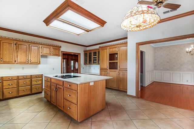 kitchen featuring a center island, ceiling fan with notable chandelier, black stovetop, ornamental molding, and decorative light fixtures