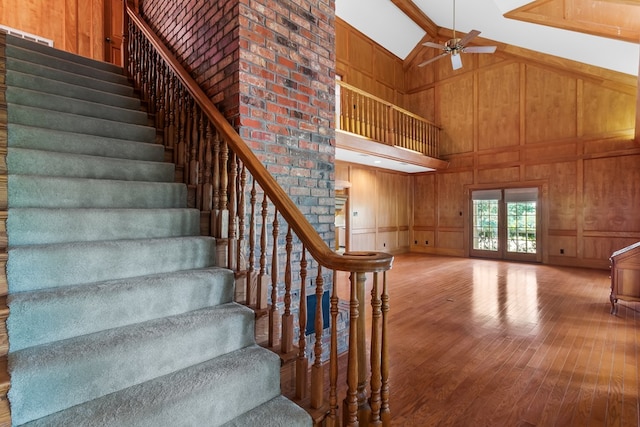 staircase with hardwood / wood-style flooring, ceiling fan, wooden walls, and high vaulted ceiling