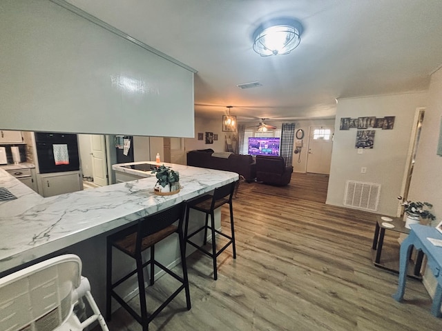 kitchen with a peninsula, a kitchen bar, visible vents, and wood finished floors