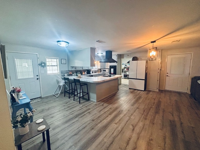 kitchen featuring decorative light fixtures, island exhaust hood, light countertops, freestanding refrigerator, and a peninsula