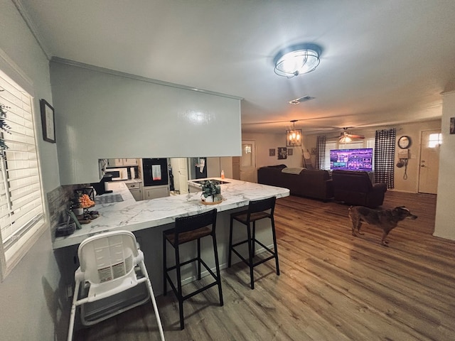 kitchen with dark wood-style flooring, white microwave, open floor plan, a peninsula, and a kitchen bar