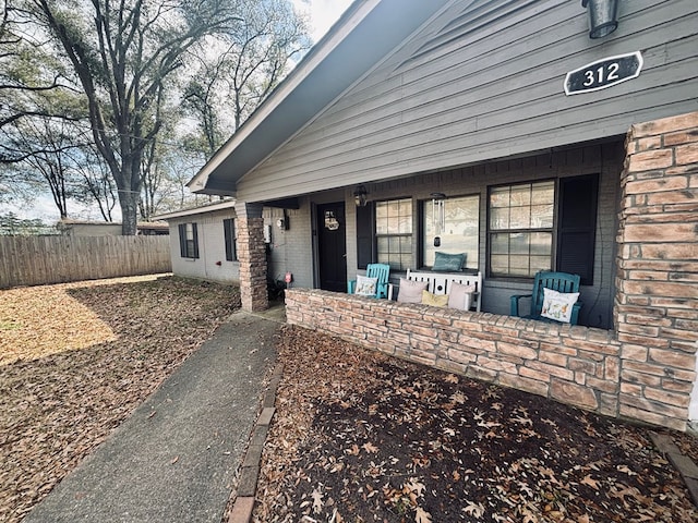 exterior space with a porch, brick siding, and fence