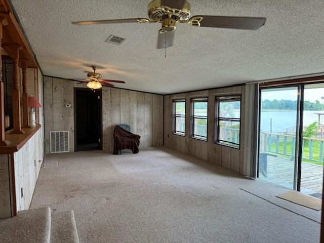 unfurnished living room with a textured ceiling, a water view, light colored carpet, and wood walls