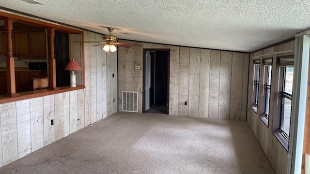 spare room with a textured ceiling, vaulted ceiling, and wood walls