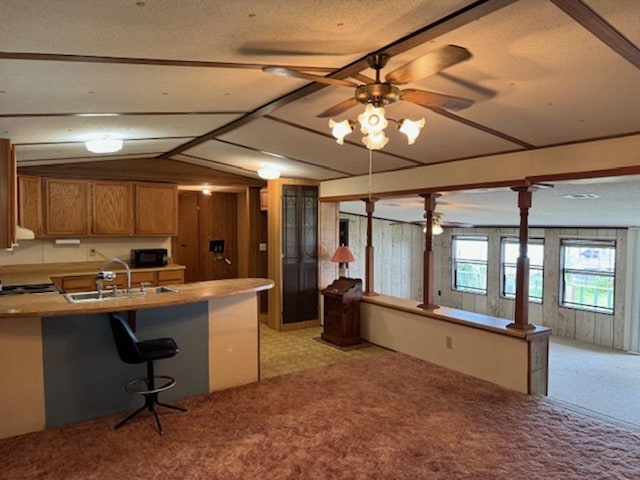 kitchen with kitchen peninsula, light carpet, ceiling fan, sink, and a breakfast bar area