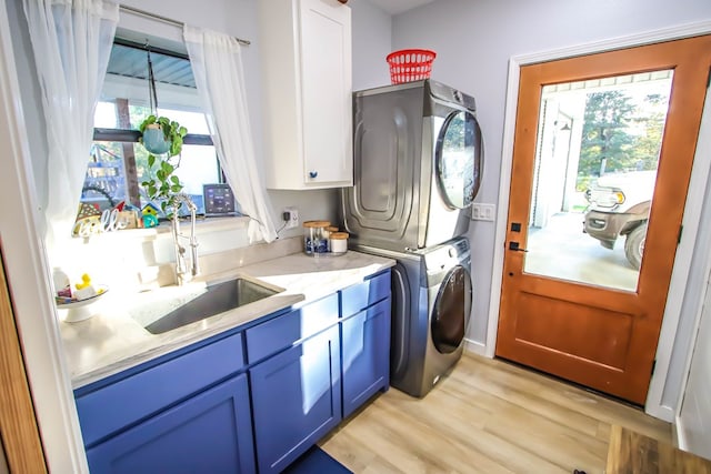 laundry room with stacked washer / dryer, light hardwood / wood-style flooring, cabinets, and sink