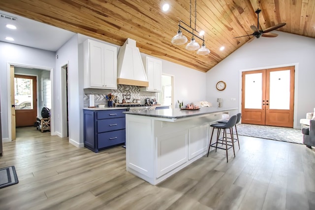 kitchen with light wood-type flooring, custom range hood, blue cabinetry, white cabinets, and hanging light fixtures