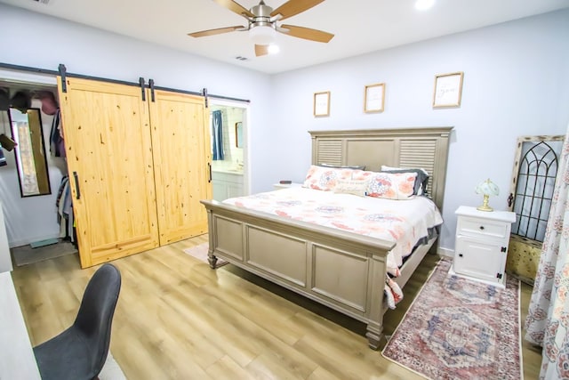 bedroom with light wood-type flooring, a barn door, ensuite bath, and ceiling fan