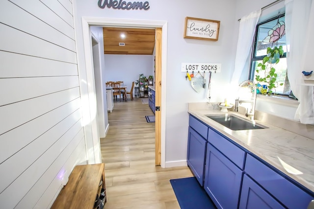 kitchen with blue cabinetry, light stone countertops, sink, wood walls, and light hardwood / wood-style floors