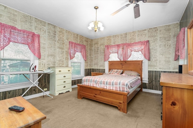 carpeted bedroom with ceiling fan with notable chandelier and wood walls