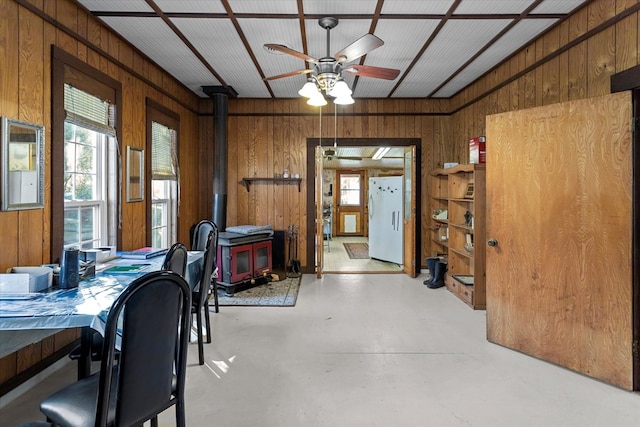 dining space featuring a wood stove, wooden walls, and ceiling fan