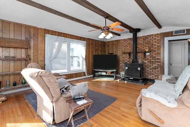 living room with wood walls, a wood stove, vaulted ceiling with beams, a textured ceiling, and wood-type flooring