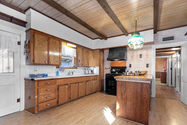 kitchen with black range with gas stovetop, light wood-type flooring, decorative light fixtures, and custom exhaust hood