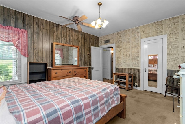 bedroom with ceiling fan with notable chandelier, wood walls, and carpet floors