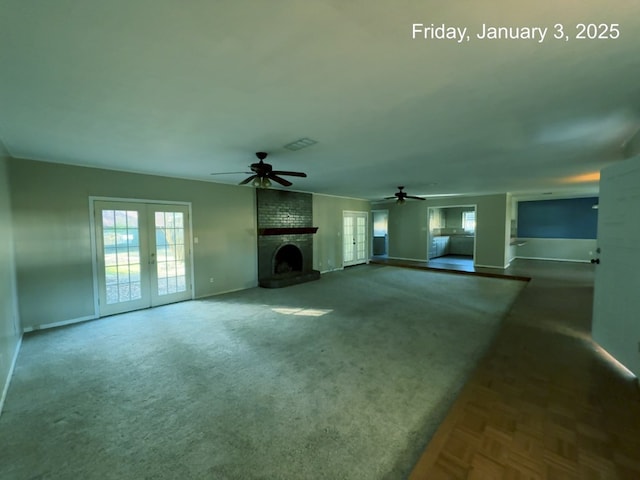 unfurnished living room with a brick fireplace, ceiling fan, carpet flooring, and french doors