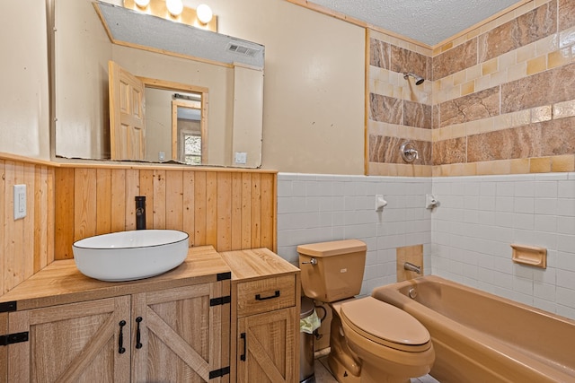 full bathroom featuring tiled shower / bath, tile walls, vanity, toilet, and a textured ceiling