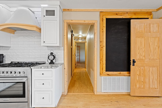 kitchen with white cabinets, light stone counters, gas range, custom range hood, and light hardwood / wood-style flooring