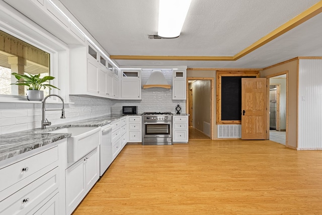 kitchen with high end stainless steel range, white dishwasher, custom range hood, light hardwood / wood-style floors, and white cabinets