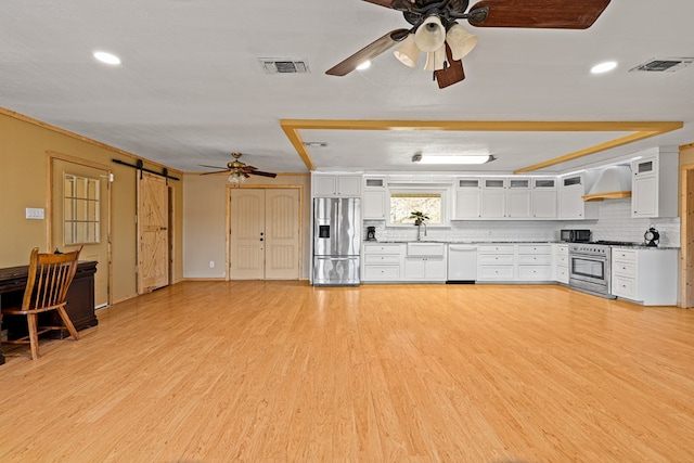 kitchen with premium range hood, white cabinetry, appliances with stainless steel finishes, a barn door, and light wood-type flooring