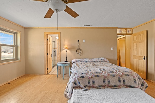 bedroom featuring ceiling fan, ensuite bathroom, a textured ceiling, and light wood-type flooring