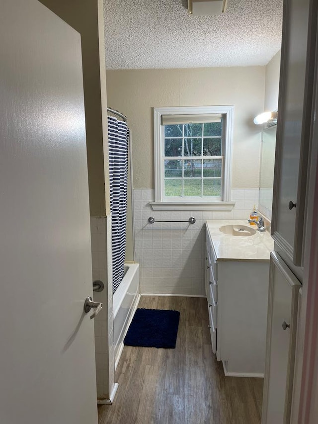 bathroom featuring hardwood / wood-style floors, a textured ceiling, shower / tub combo with curtain, vanity, and tile walls