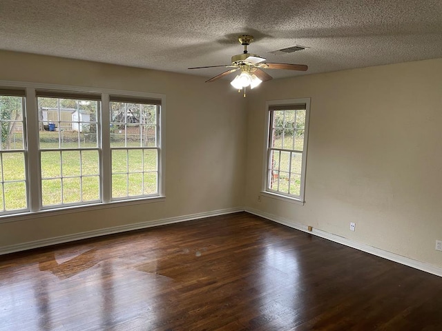 empty room with a textured ceiling, dark hardwood / wood-style flooring, and a healthy amount of sunlight