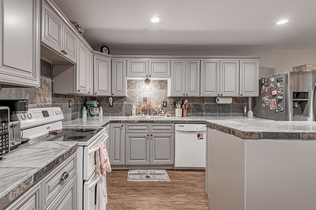 kitchen with white appliances, light hardwood / wood-style floors, tasteful backsplash, and sink