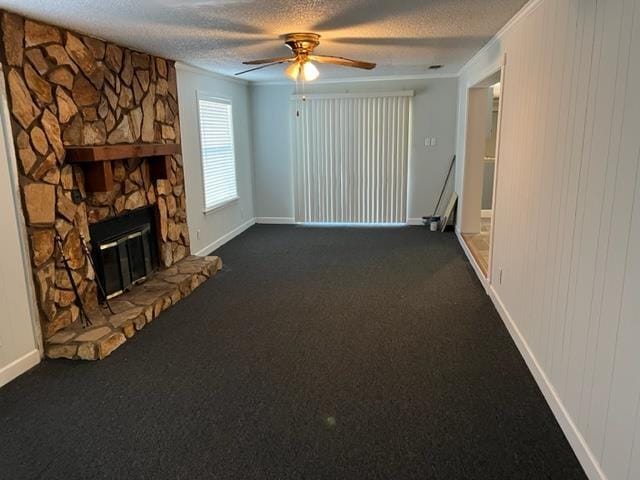 unfurnished living room with dark carpet, crown molding, ceiling fan, a textured ceiling, and a fireplace