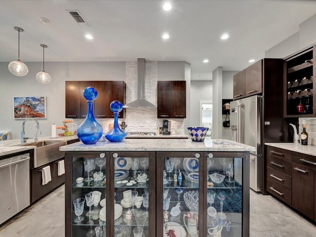 kitchen featuring appliances with stainless steel finishes, backsplash, decorative light fixtures, dark brown cabinets, and wall chimney exhaust hood