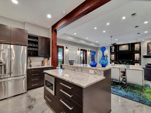 kitchen with appliances with stainless steel finishes, a tray ceiling, dark brown cabinets, light stone counters, and a center island