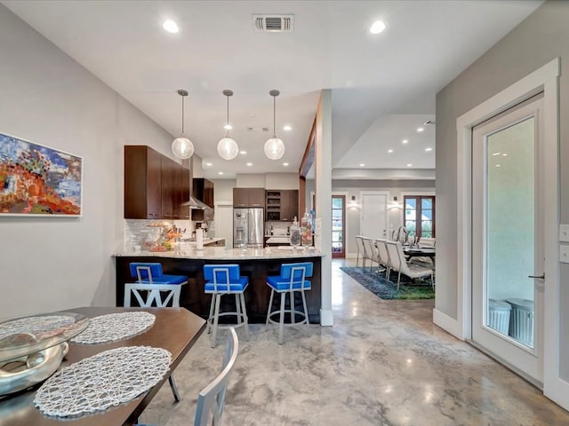 kitchen with a kitchen bar, kitchen peninsula, stainless steel refrigerator with ice dispenser, tasteful backsplash, and dark brown cabinets