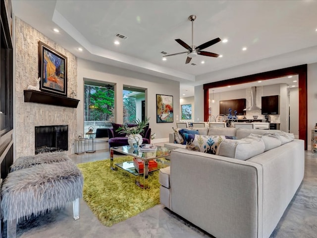 living room featuring ceiling fan, a fireplace, and a tray ceiling