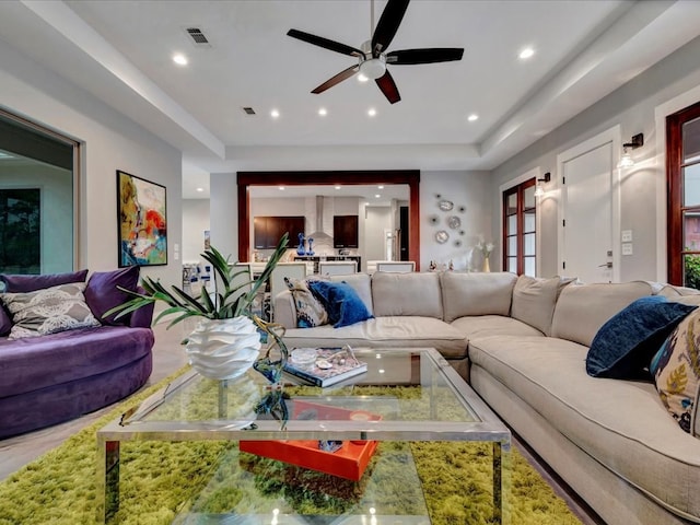 living room featuring ceiling fan and a raised ceiling