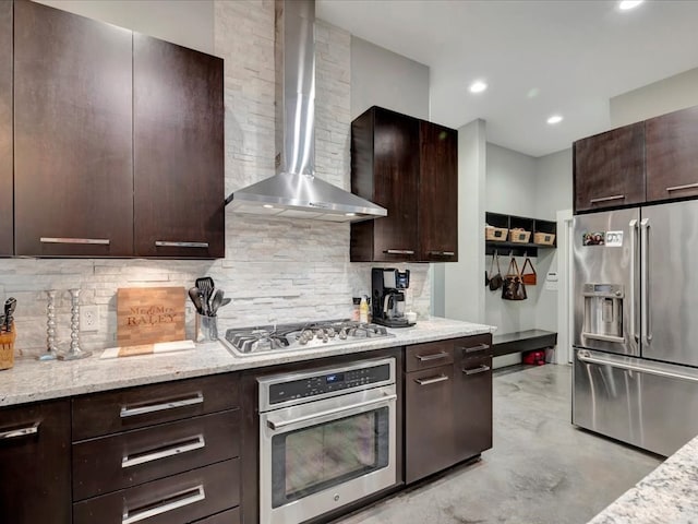 kitchen with appliances with stainless steel finishes, decorative backsplash, wall chimney range hood, light stone counters, and dark brown cabinetry