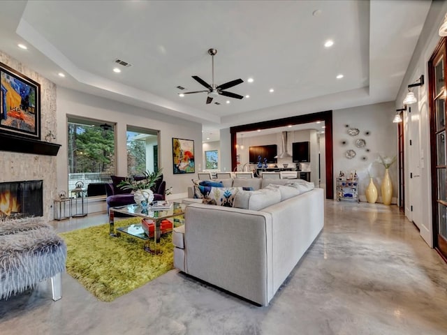 living room featuring ceiling fan, a tray ceiling, and a fireplace