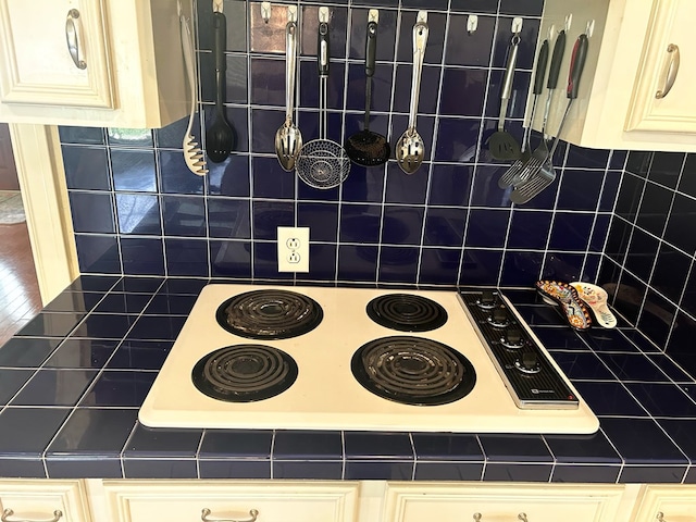 kitchen featuring cream cabinetry, tile counters, white electric stovetop, and tasteful backsplash