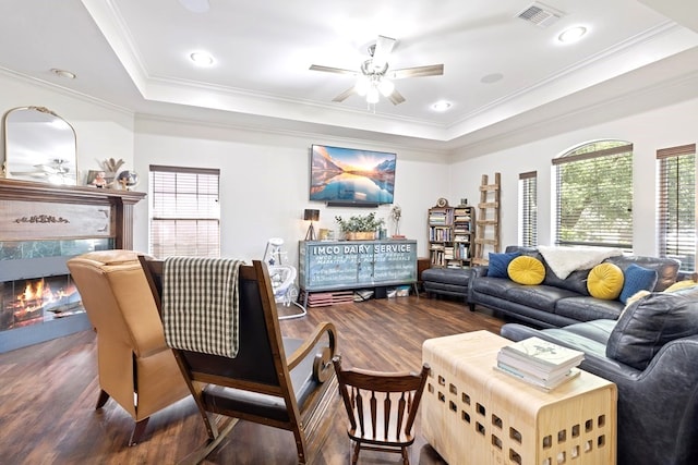 living room featuring a raised ceiling, dark wood-type flooring, and ornamental molding